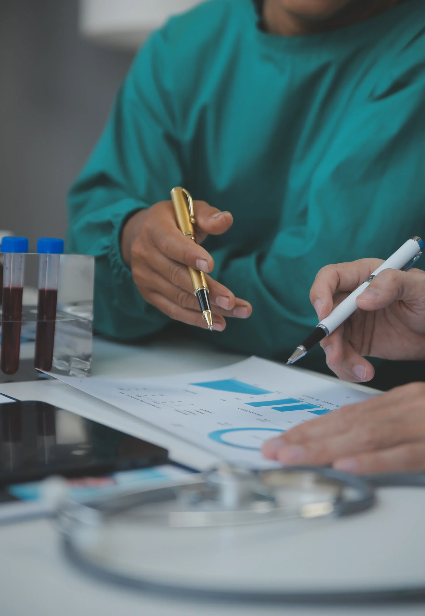 Healthcare staff pointing at printed charts on a desk during a manual compliance screening process.